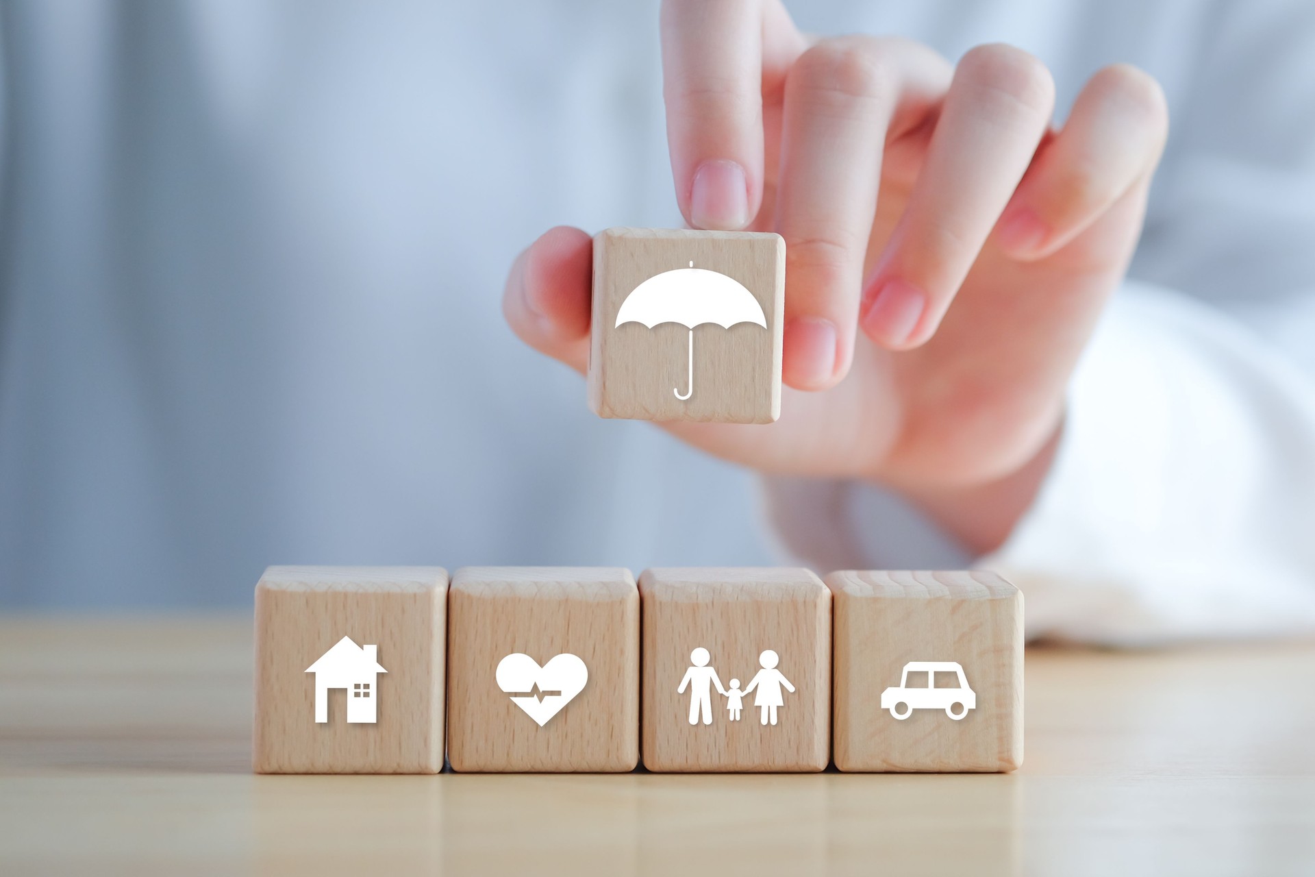 Concepto de seguro. Protección ante una posible eventualidad. Icono de paraguas sostenido a mano e icono de casa, automóvil, familia y salud en un bloque de madera para garantizar el concepto de vida.